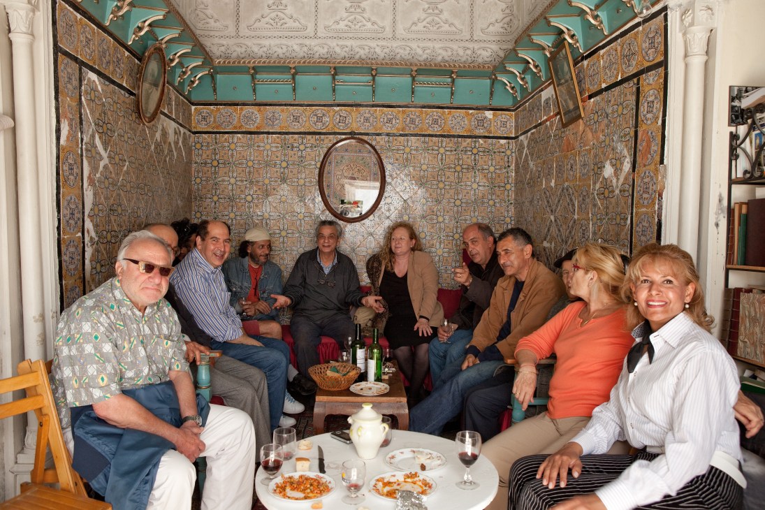 Mohamed Bennani sits with a group of intellectuals in a tiled Tunisian room during a couscous lunch.