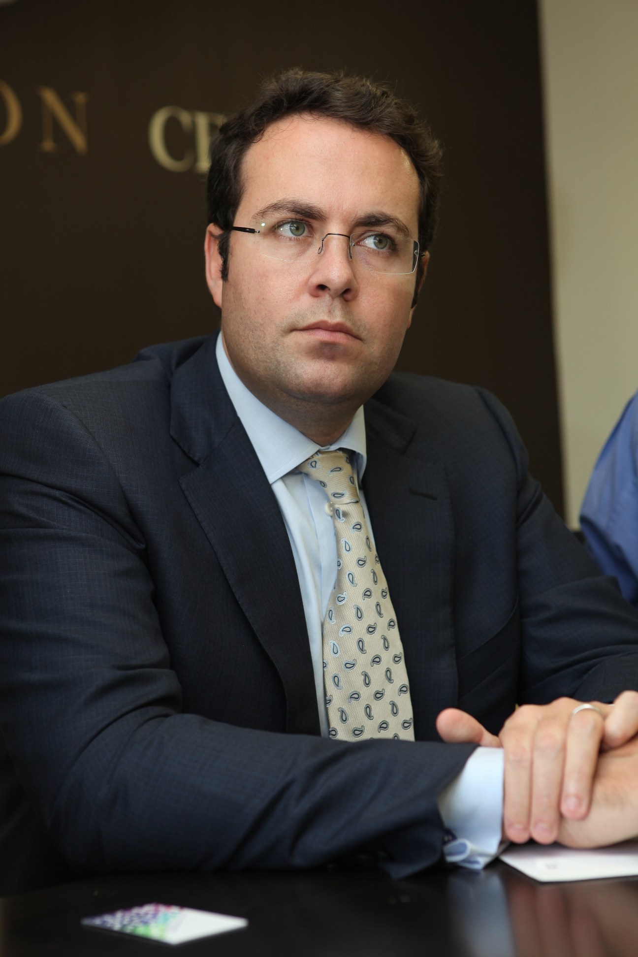 Bank of Palestine CEO Hashem Shawa wearing glasses and a dark suit with patterned tie at a formal event.