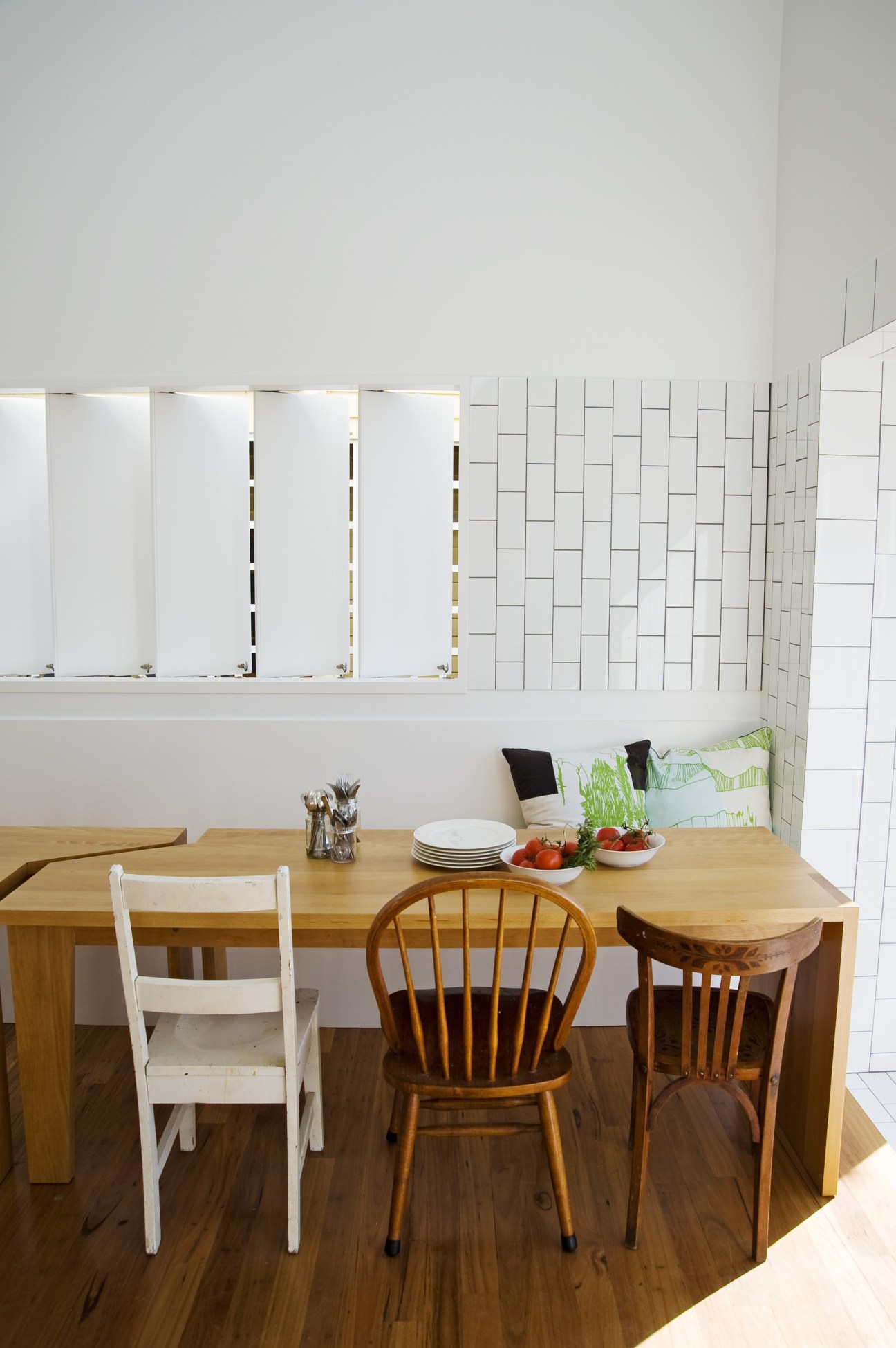 Dining room with wooden table, built-in bench, and white subway tile walls with ventilation details.