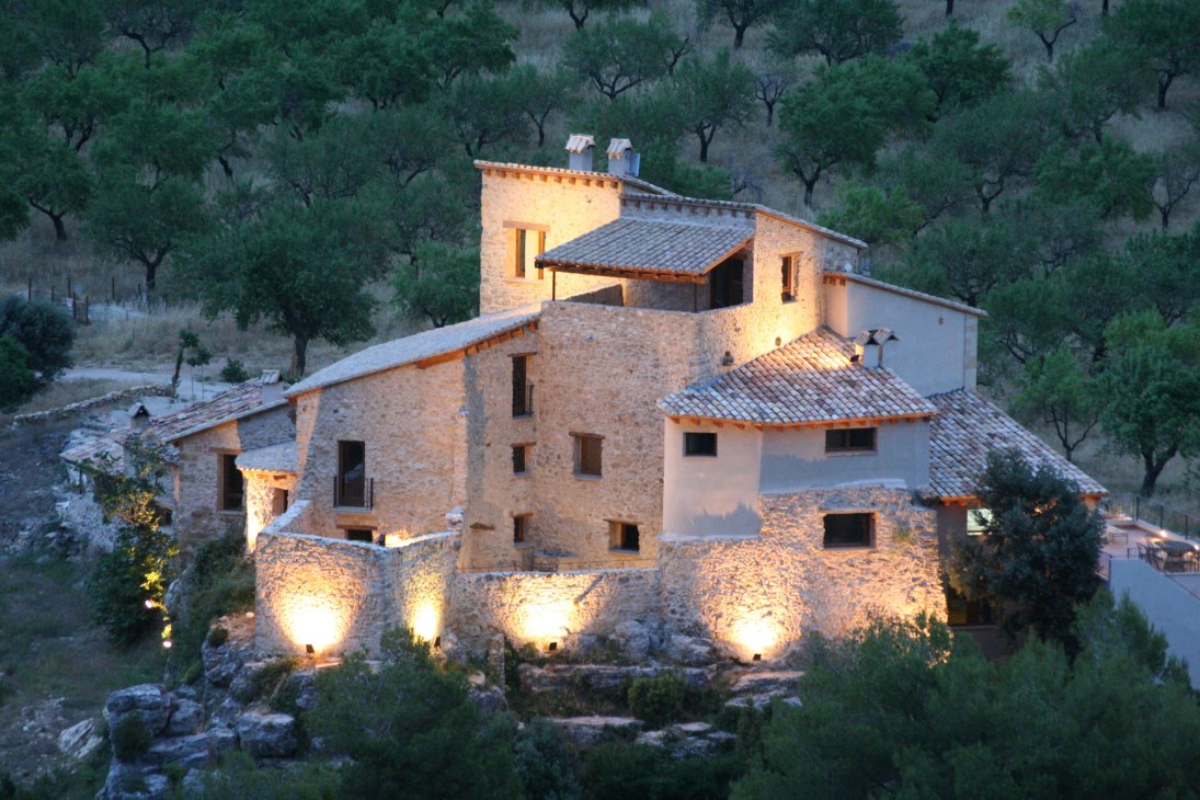 Illuminated medieval stone farmhouse nestled among olive trees in rural Spain at dusk.