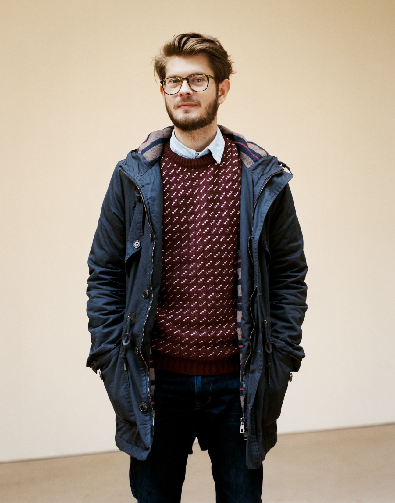 Portrait of Benjamin Renoux, a male student wearing glasses, burgundy patterned sweater, and navy parka jacket against a beige background.