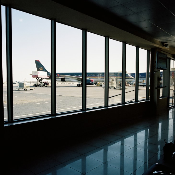 View from airport terminal windows overlooking tarmac with Royal Jordanian aircraft and ground support equipment.