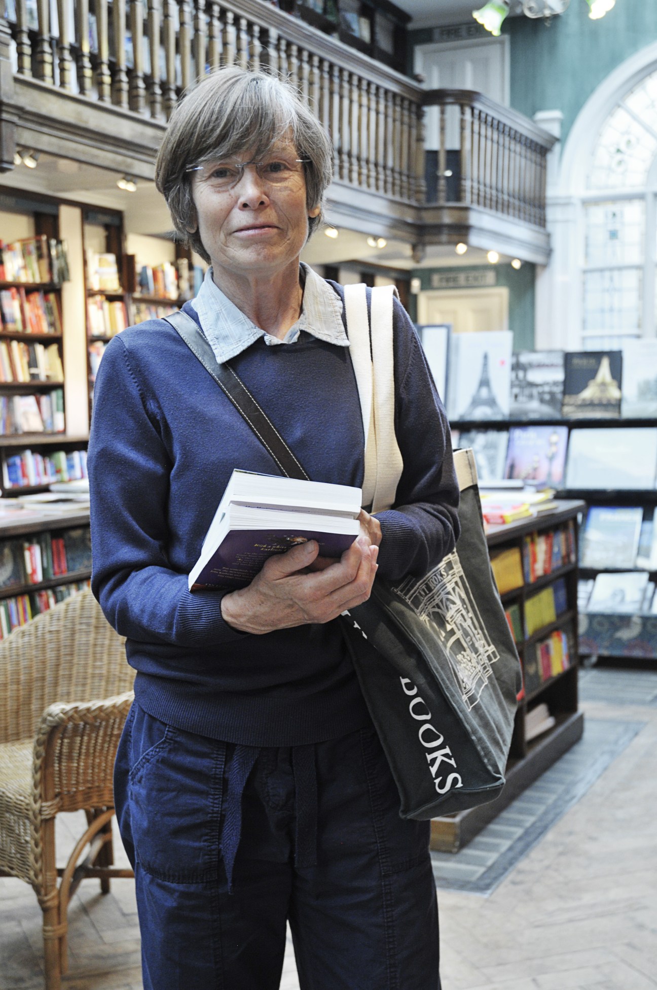 Caroline Cochrane, a customer, stands in Daunt Books holding books with the bookshop's interior visible behind her.
