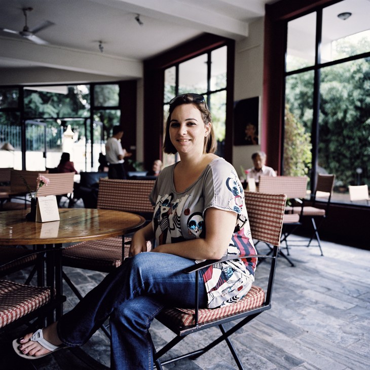 Rachael Manley, owner of a new art café, sits at a table in her modern Kathmandu restaurant with large windows overlooking greenery.