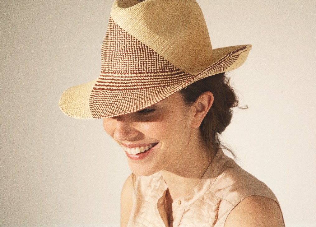Woman wearing a Borsalino straw Panama hat with a distinctive wave emblem pattern, smiling against a neutral background.