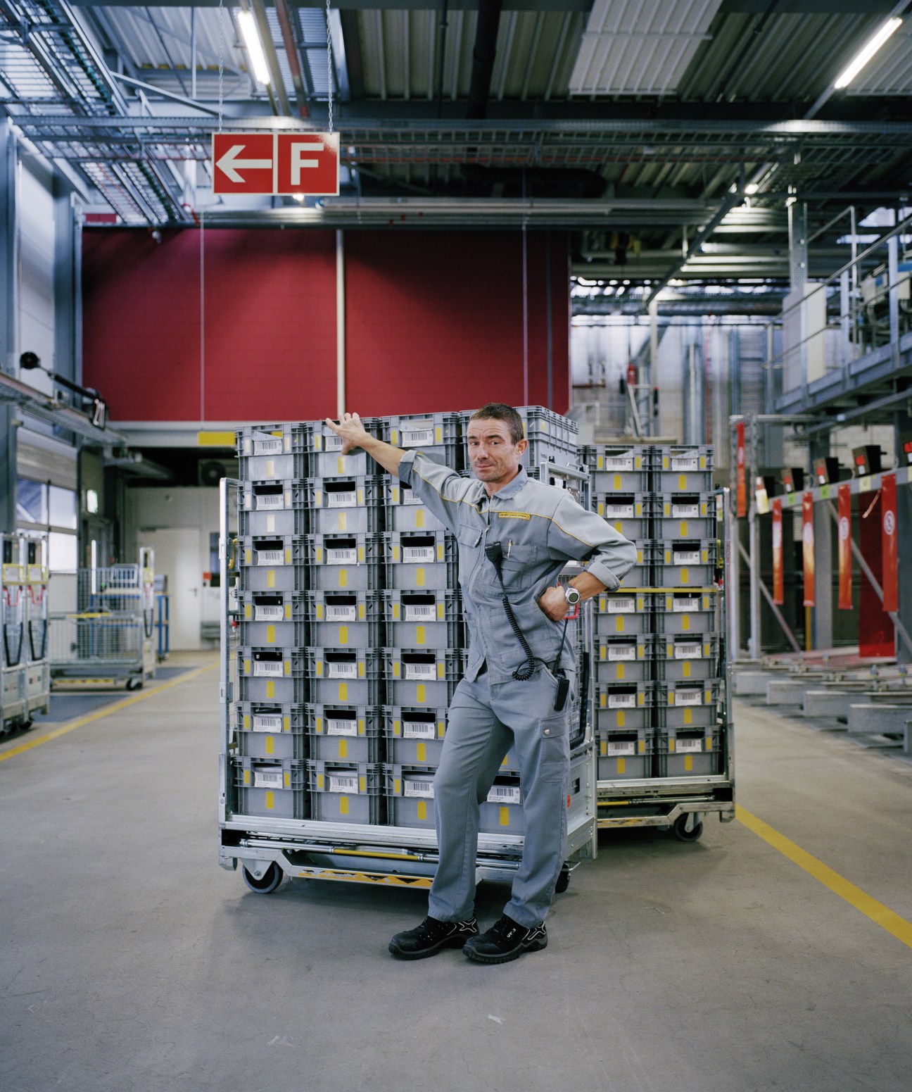 A Swiss Post worker in gray uniform stands beside large mail sorting crates at Härkingen sorting office.