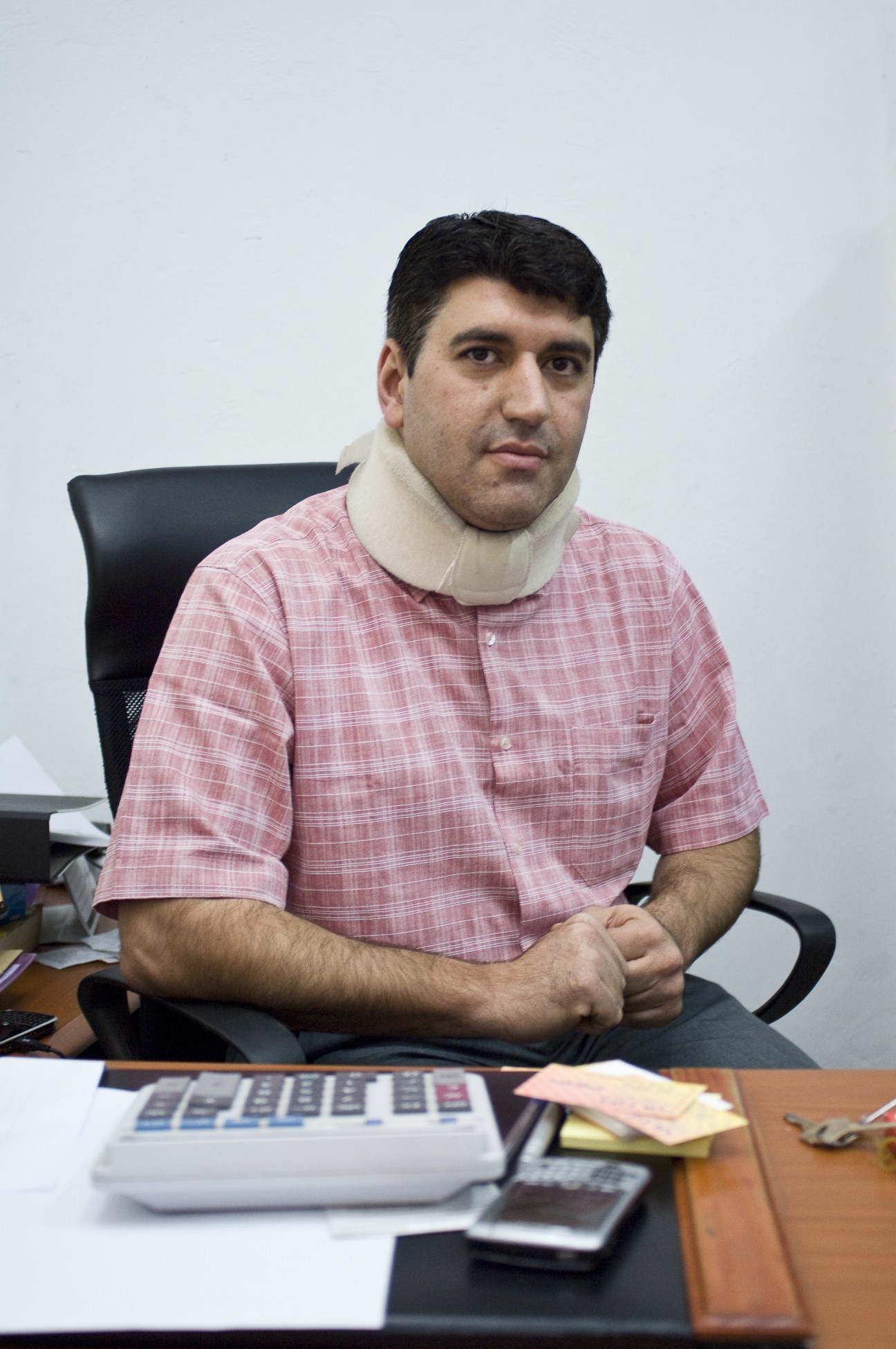 Bilal Bakri, a Lebanese entrepreneur wearing a pink checkered shirt and white neck brace, seated at an office desk.
