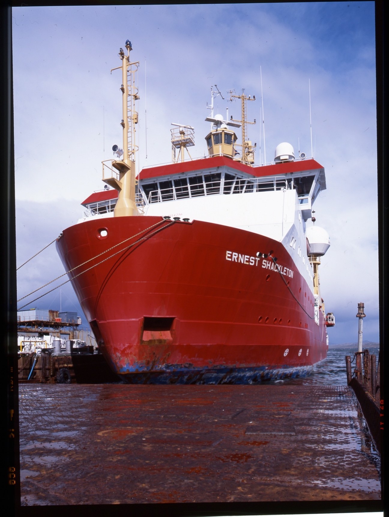 The RRS Ernest Shackleton, a red and white supply ship operated by the British Antarctic Survey, docked at port.