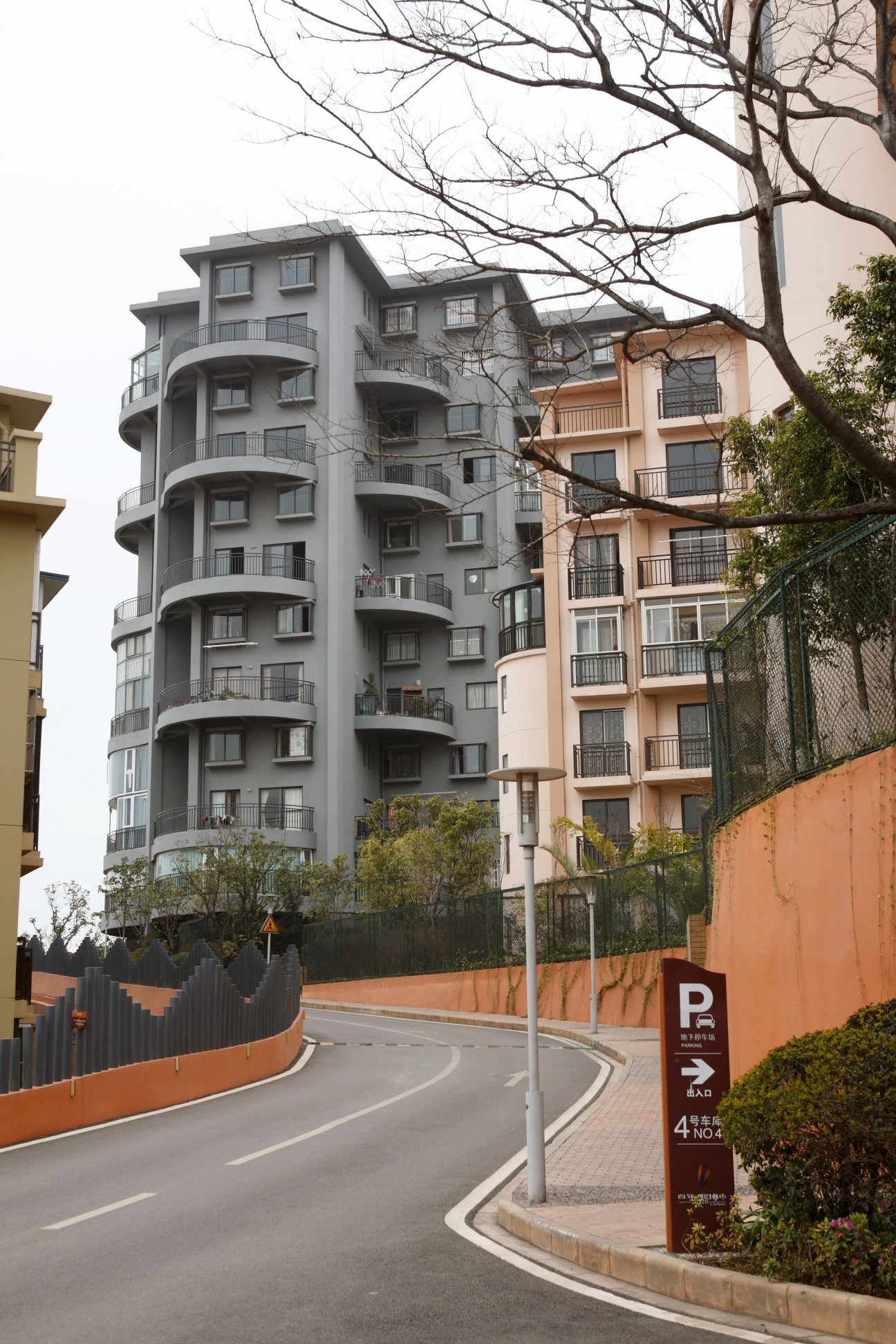 Modern apartment buildings with curved balconies and varied pastel facades alongside a parking sign.