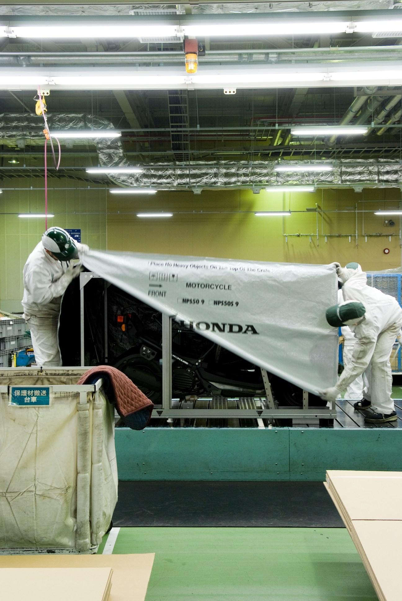 Factory workers wrapping a Honda motorcycle front section in protective plastic at the Kumamoto facility.