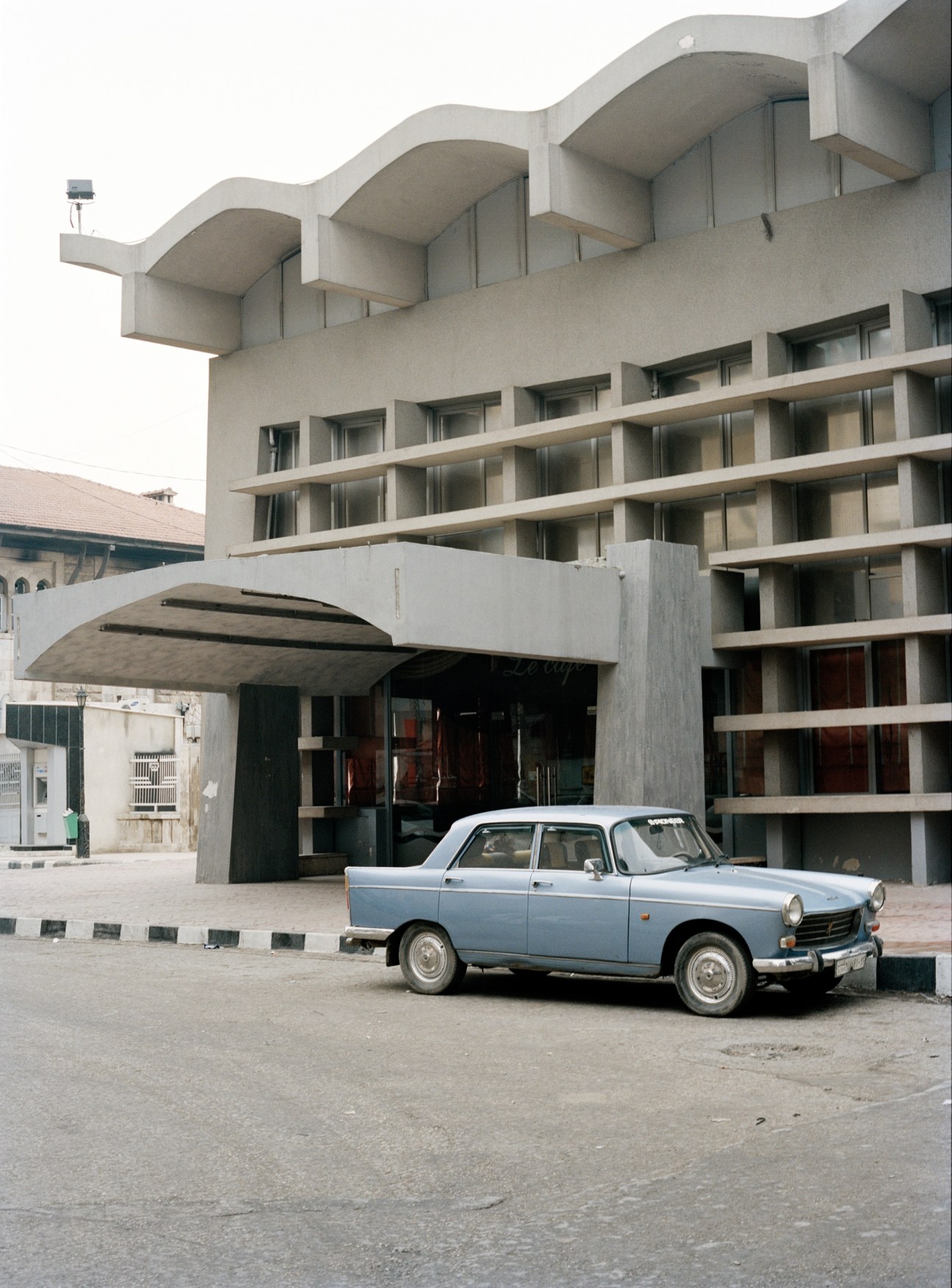 Blue vintage car parked in front of a modernist concrete building with curved balconies.