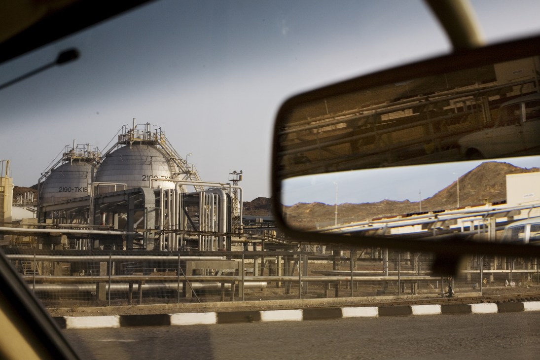 Industrial oil refinery with large storage tanks viewed through a vehicle's side mirror.