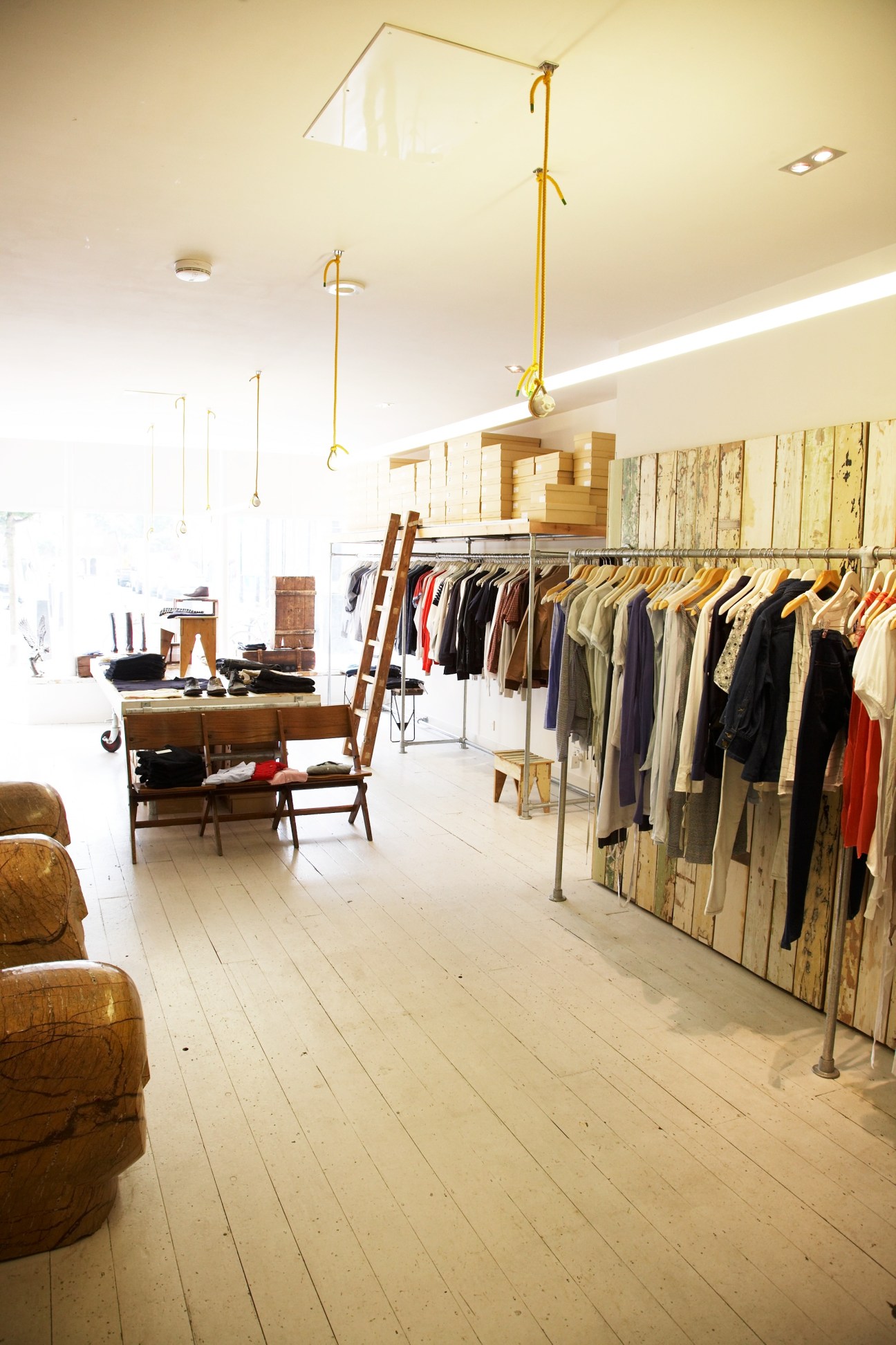 Interior of Folk Clothing store with wooden floors, brass fixtures, clothing rack, and vintage furniture.