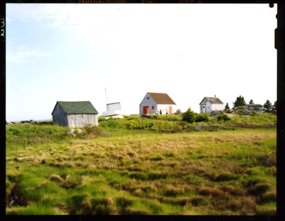 Historic colorful cottages and fishing buildings scattered across green fields in rural Nova Scotia.