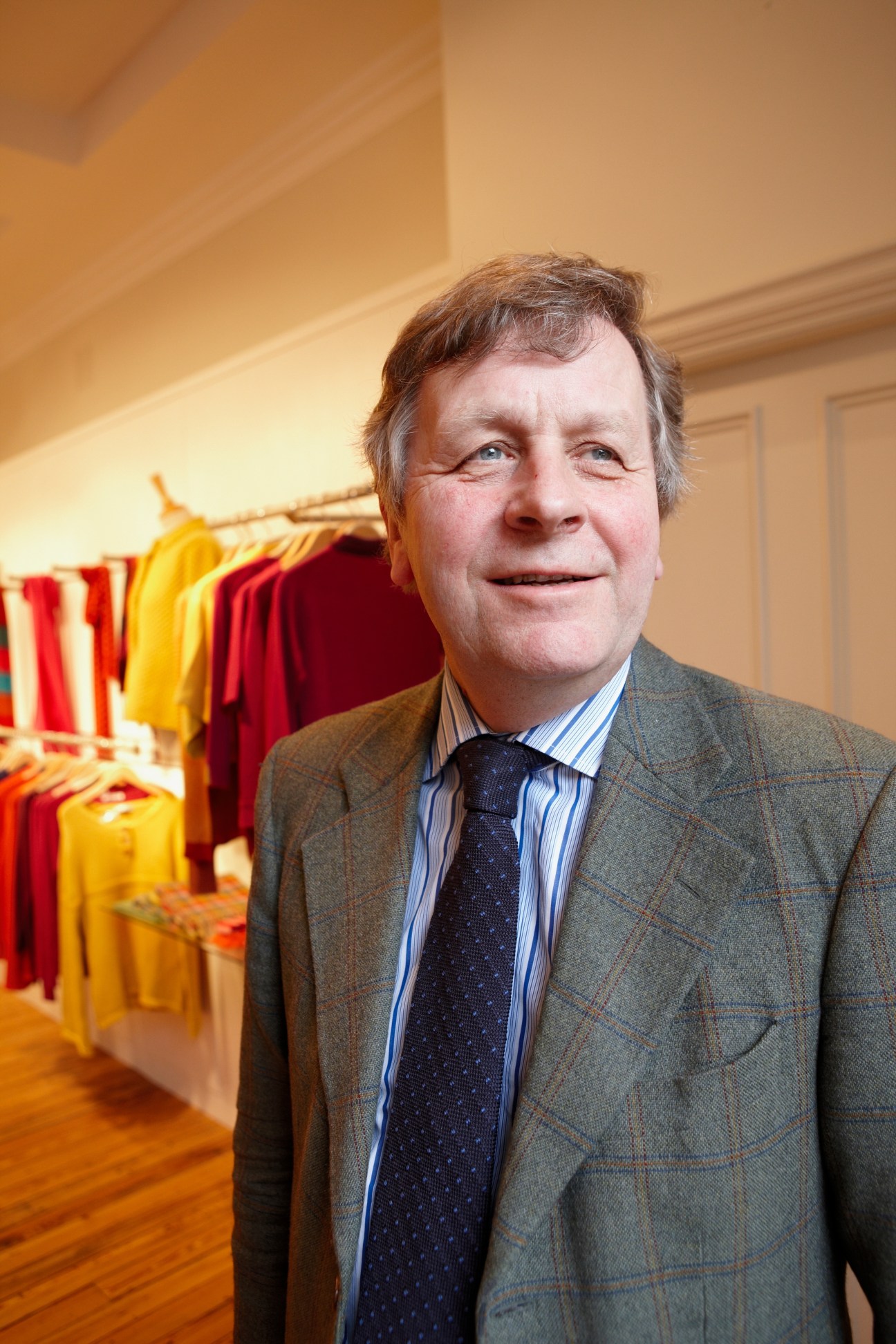 James Sugden, managing director of Johnstons Cashmere, stands in the showroom with colorful cashmere fabrics on display behind him.
