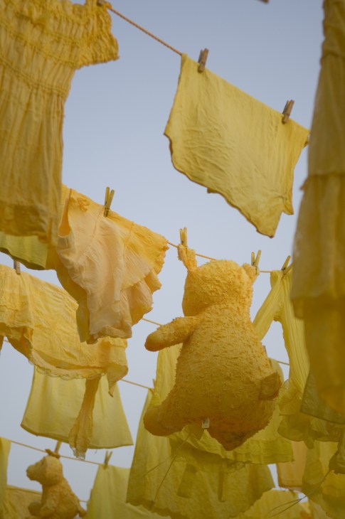 Yellow fabric and teddy bear shapes hung on clothesline against blue sky.