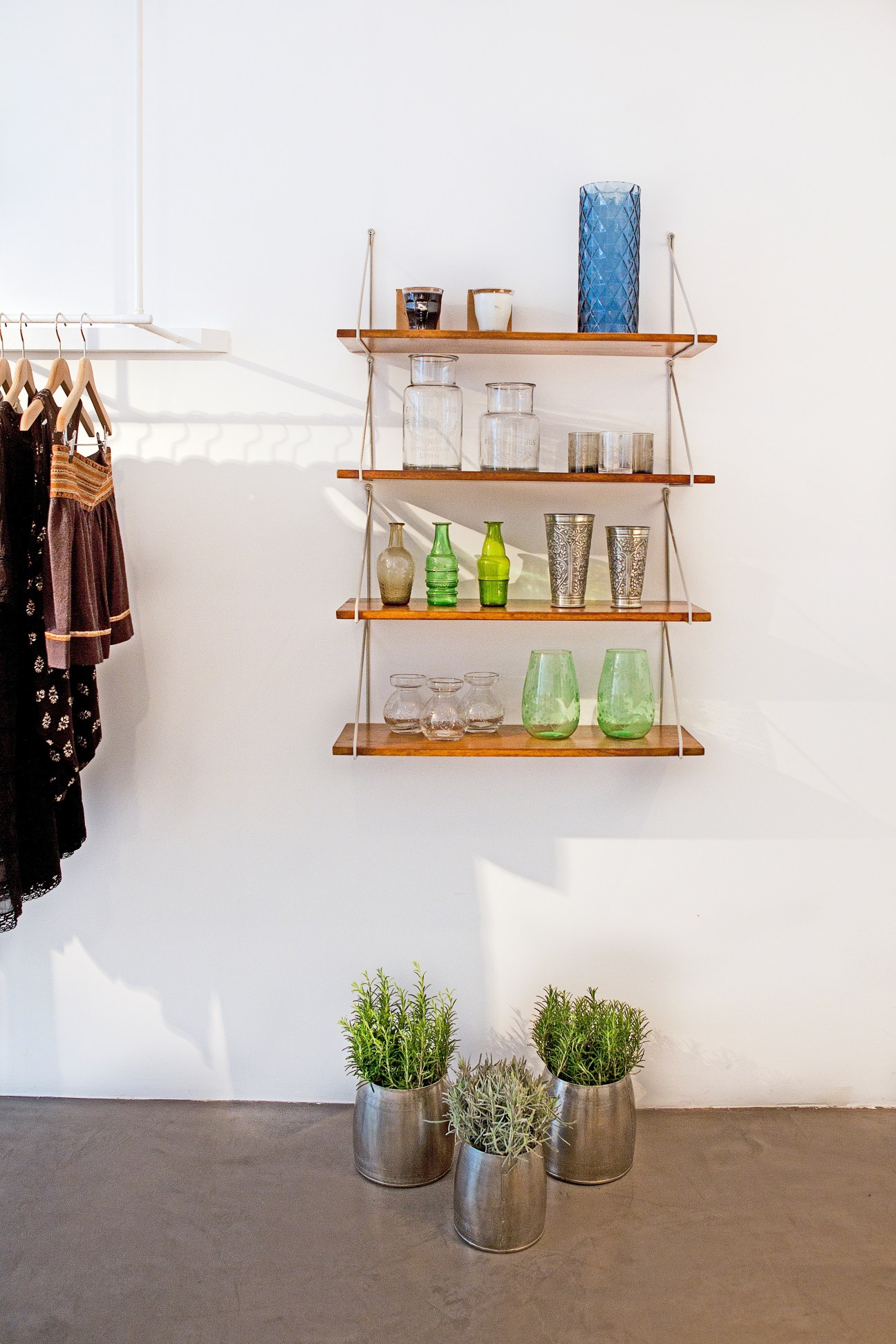 Interior of Aimé shop displaying wooden shelves with glassware and plants, clothing racks on left.