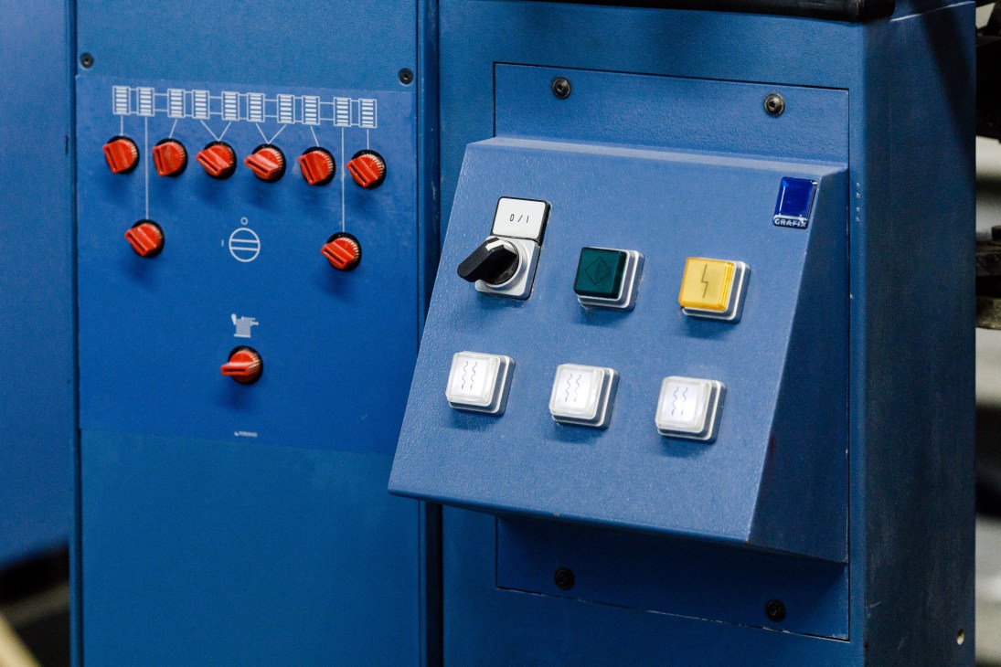 Blue industrial control panel with red knobs and switches at Pantone headquarters.
