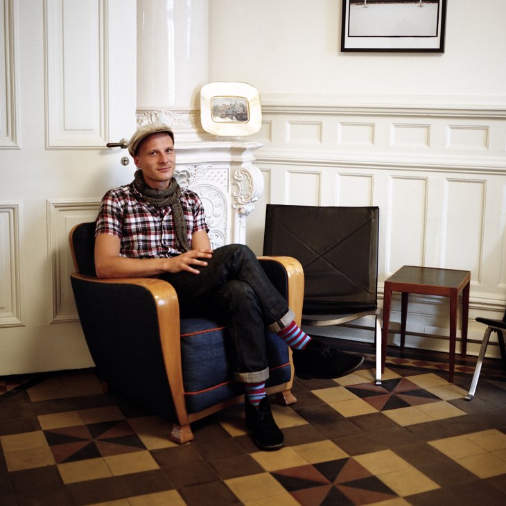 Joakim Levin of Nudie jeans sitting in a mid-century modern chair in an elegant white panelled room.
