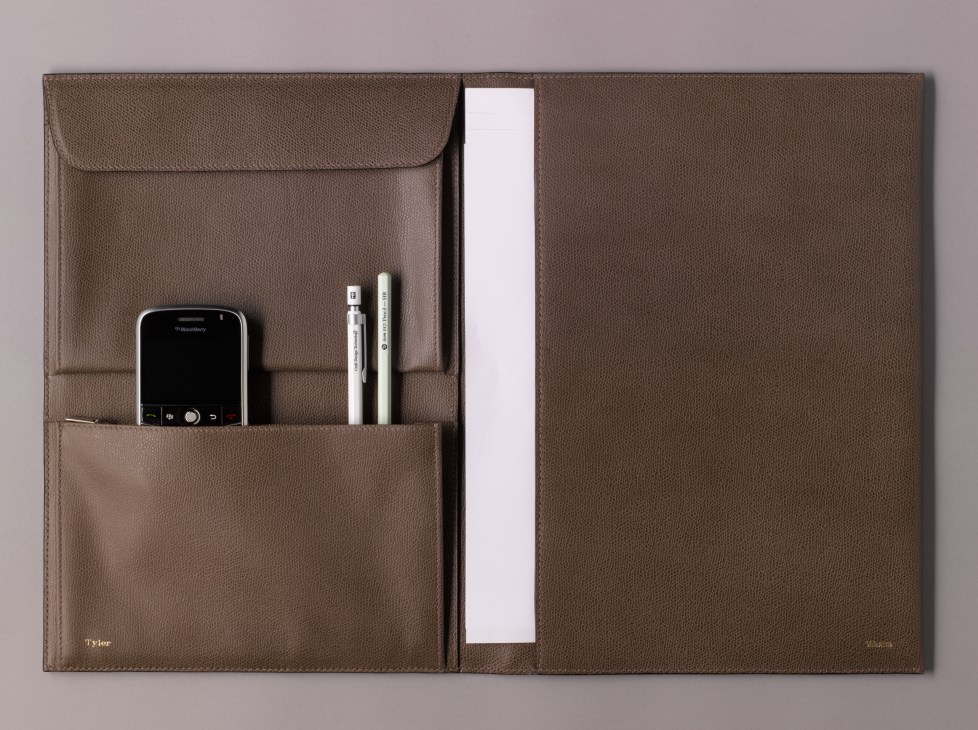 Brown leather Valextra portfolio open displaying compartments with phone, pens and papers.