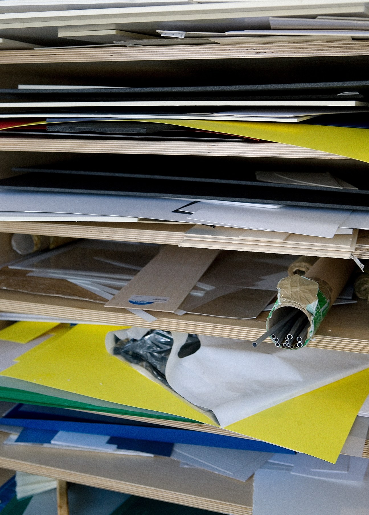 Shelves containing stacked architectural model materials including papers, fabrics, and metal tubes in various colors.