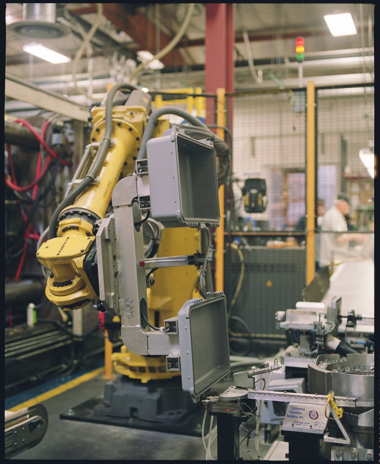 Yellow industrial robot arm moving grey Pelican cases along a manufacturing production line