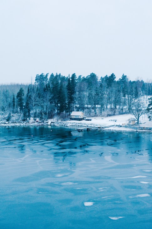 Frozen lake with a cottage and forest in winter landscape near Stockholm.