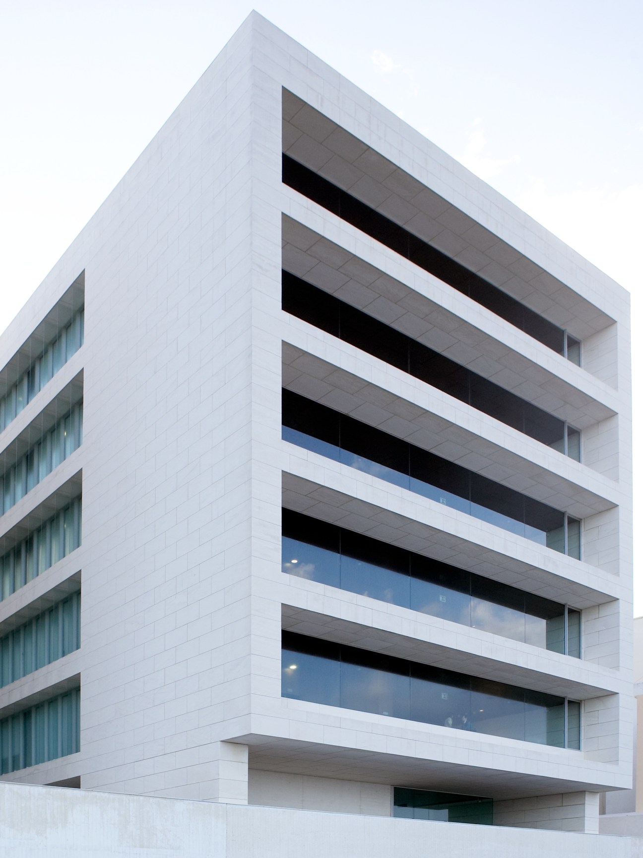 Modern white building with stacked horizontal balconies and large windows against a clear sky.
