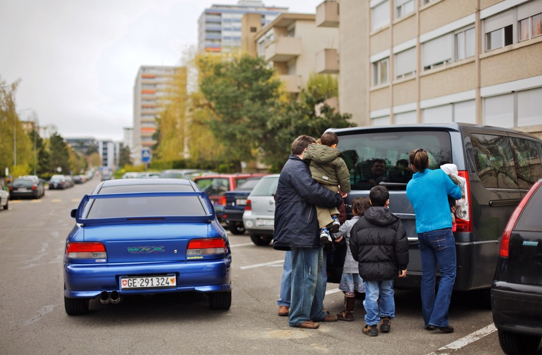 Robert Couturier stands with his family beside his blue Subaru Impreza in a parking lot.