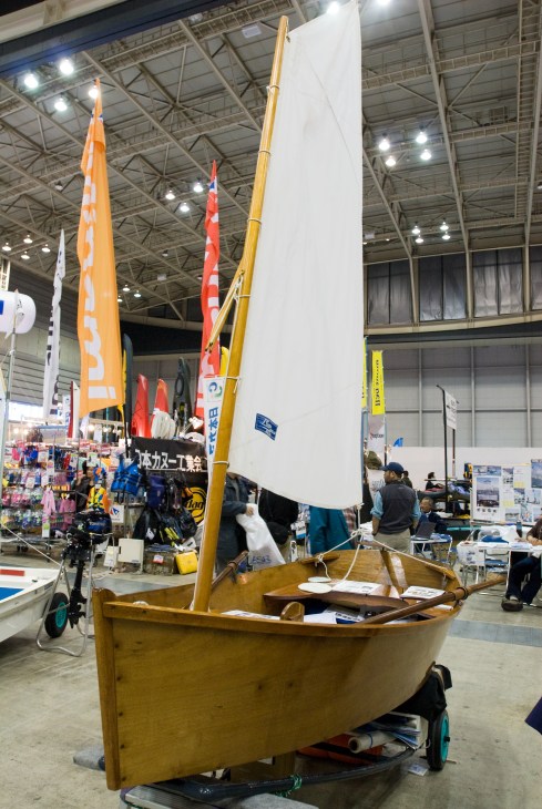 Wooden sailboat with white sail and colored sails displayed indoors at Japan International Boat Show
