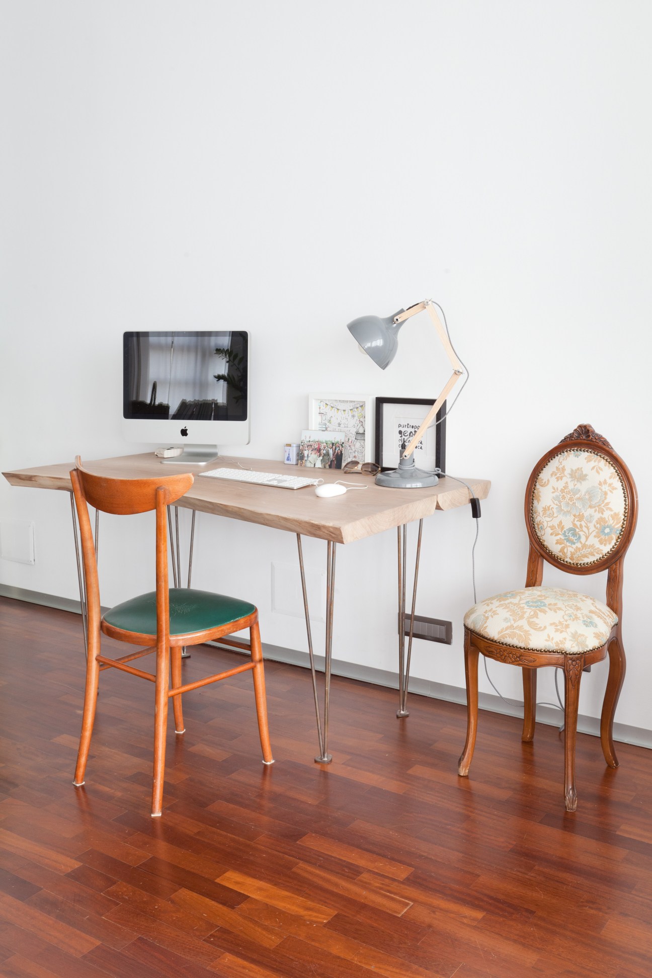 Study workspace with wooden desk, orange chair, ornate wooden chair, and desk lamp in minimalist interior.
