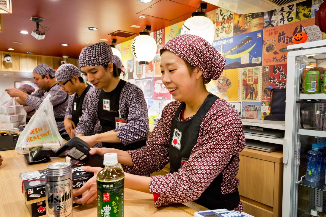 Staff in traditional patterned uniforms and headwear serve customers at Ekibenyammatsuri bento box shop in Tokyo.