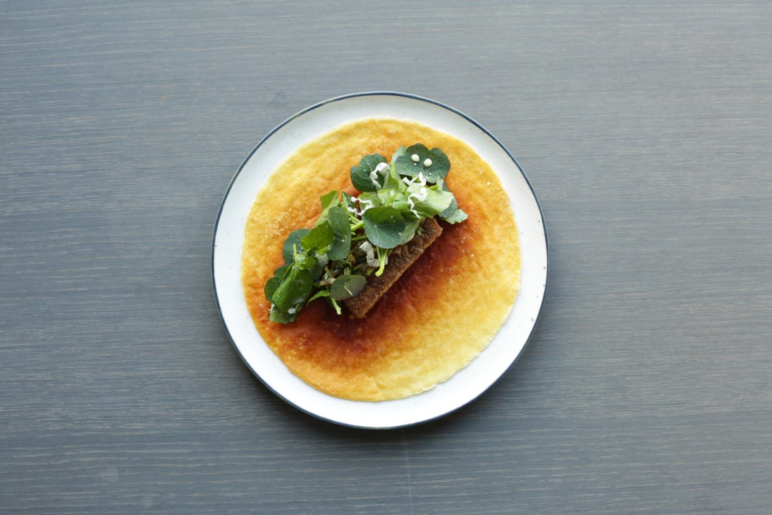 A plate of food at 108 restaurant in Copenhagen featuring a piece of meat with greens on a golden crepe.