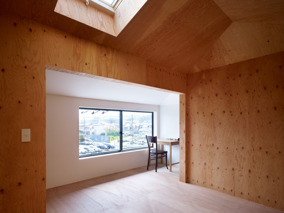 Interior of a wooden room with large windows overlooking a cityscape, featuring a desk and chair.