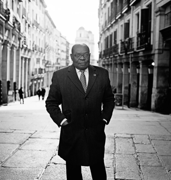 Severo Moto Nsa stands in a Madrid street wearing a dark suit and striped tie, hands in pockets.