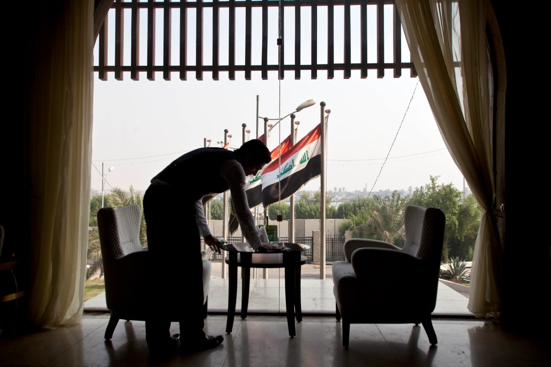 Waiter bowing at Basra International Hotel with Iraqi flag visible through window