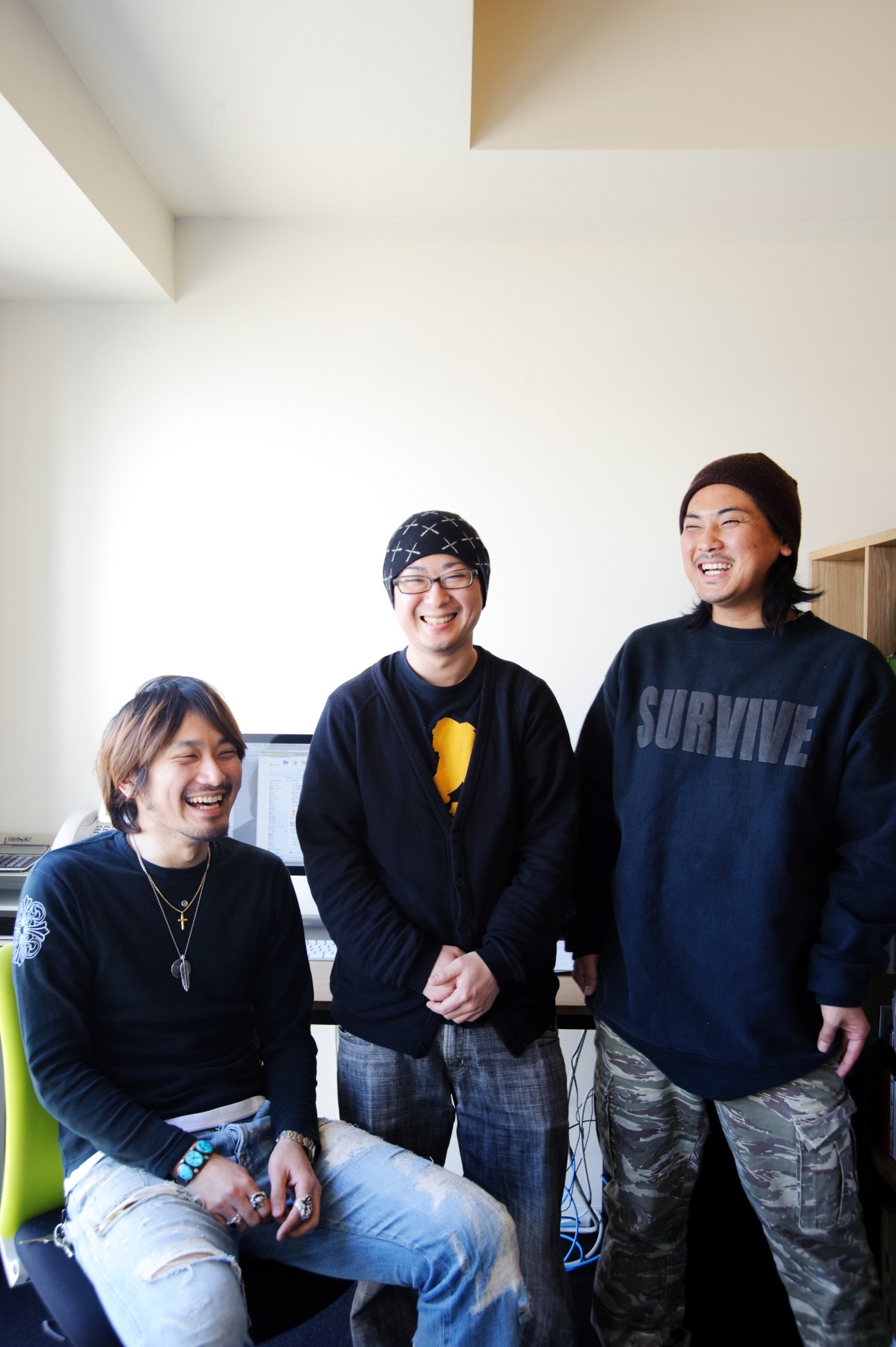 Three smiling men standing in a bright white office space with modern architectural ceiling details.