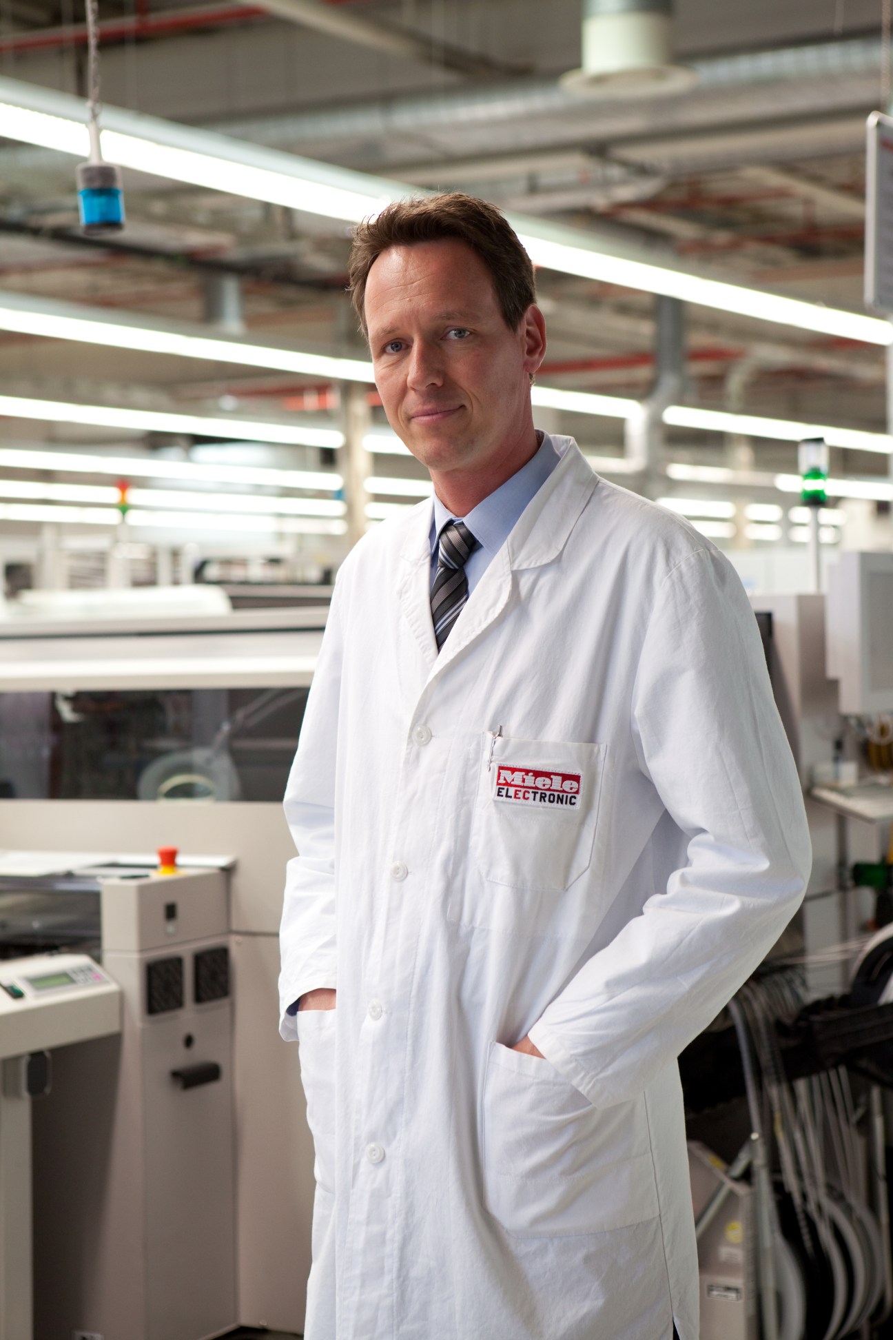Dr Rüdiger Hellenkamp wearing a white Miele lab coat stands in the electronics manufacturing facility at Gütersloh.