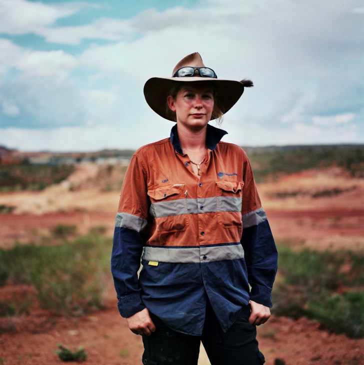 Lisa Pearce, a trainee driller, stands in work gear with an Akubra hat in the Pilbara landscape.