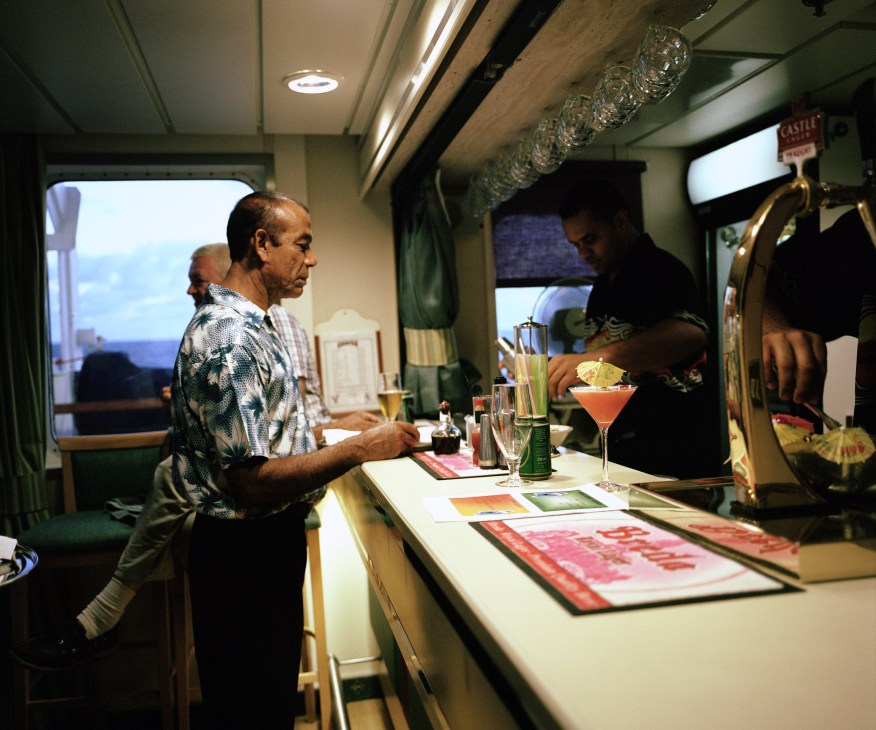 Passengers enjoying cocktails at a bar inside the RMS St Helena's sun lounge.