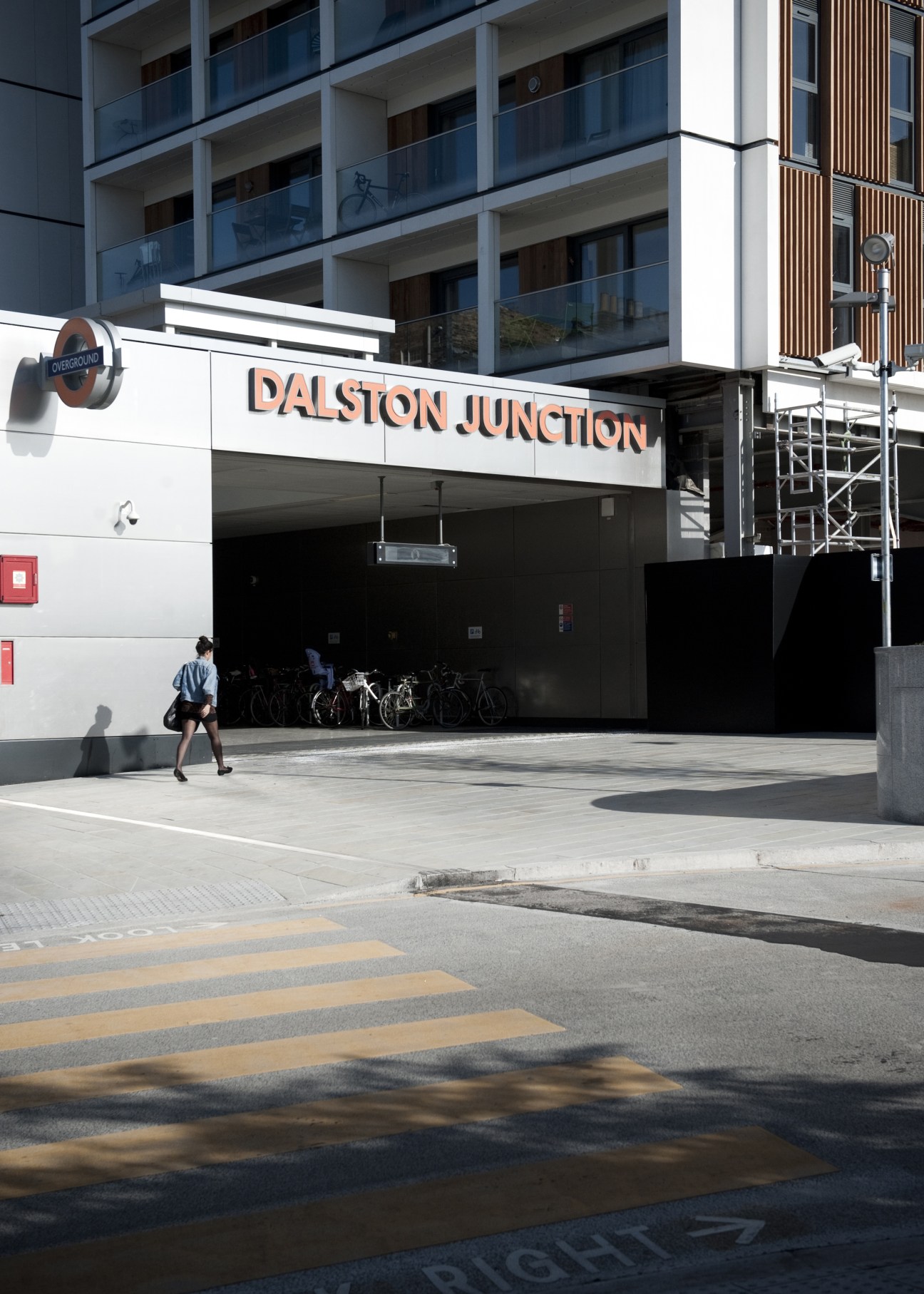 Dalston overland station entrance with modern residential building above and cyclist passing by.