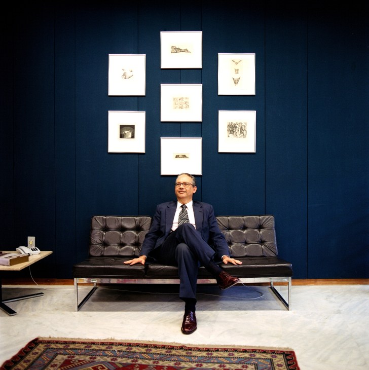 Communications department director Hélio Vitor Ramos Filho seated on a modern black leather sofa in a minimalist office with deep blue walls and framed artworks.