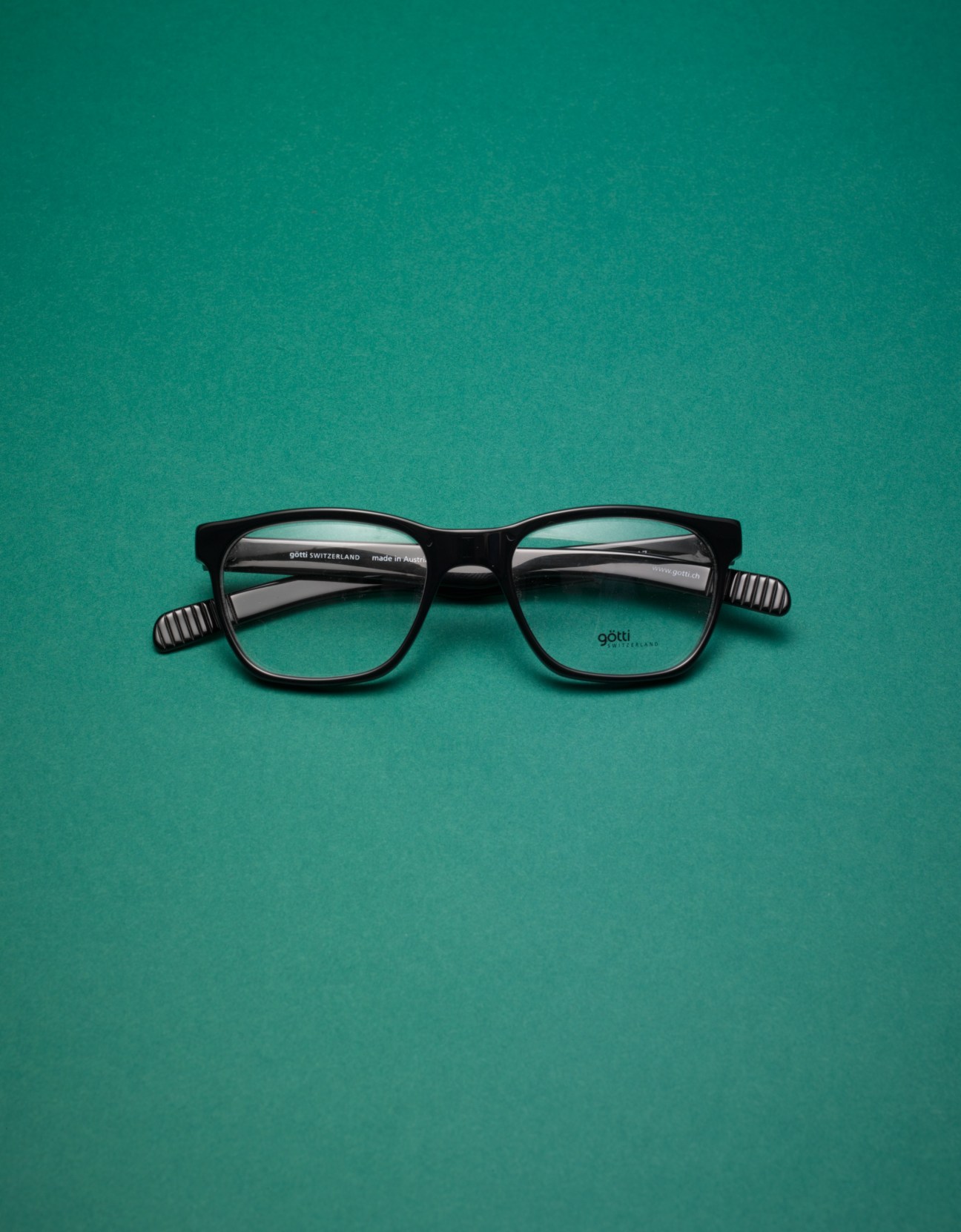 Black Gotti Ralph unisex eyeglasses with striped temples on a teal background.