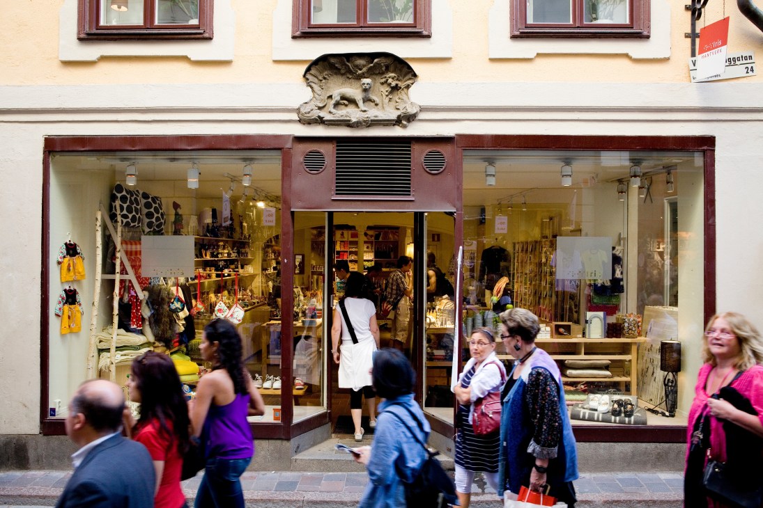 Iris Hantverk storefront in Gamla Stan with red-framed windows displaying brushes and crafts, pedestrians walking past.