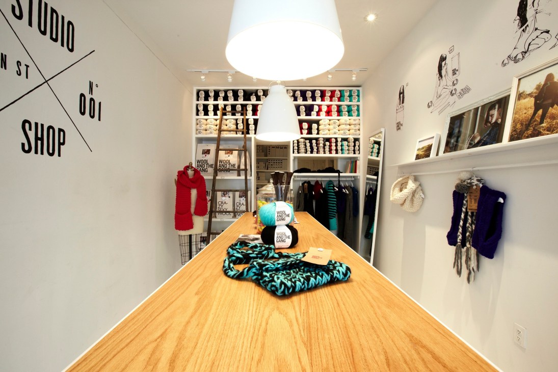 Interior of Wool and the Gang knitwear shop in New York with wooden counter, colorful yarn displays, and knitted garments.