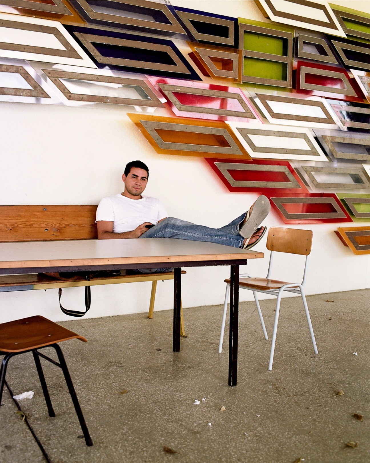 Student sitting on a bench at the University of the Netherlands Antilles with colorful picture frames on the wall behind him.