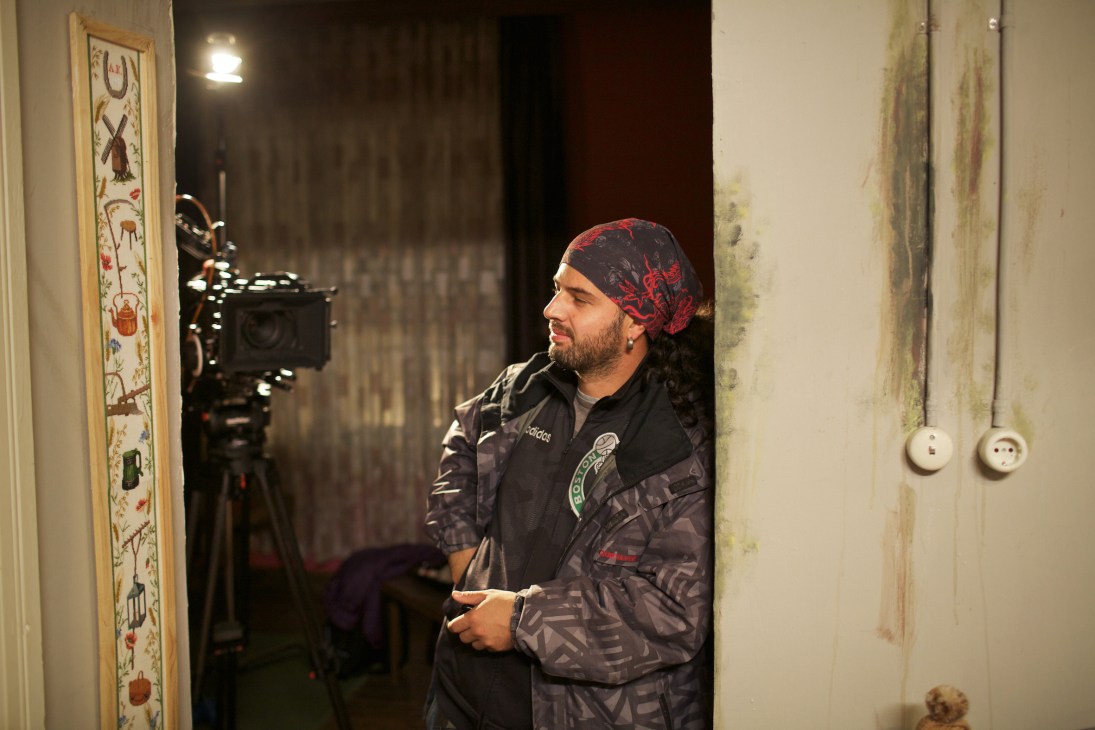 Crew member wearing a red patterned headscarf takes a break beside camera equipment on a Turkish drama series film set.