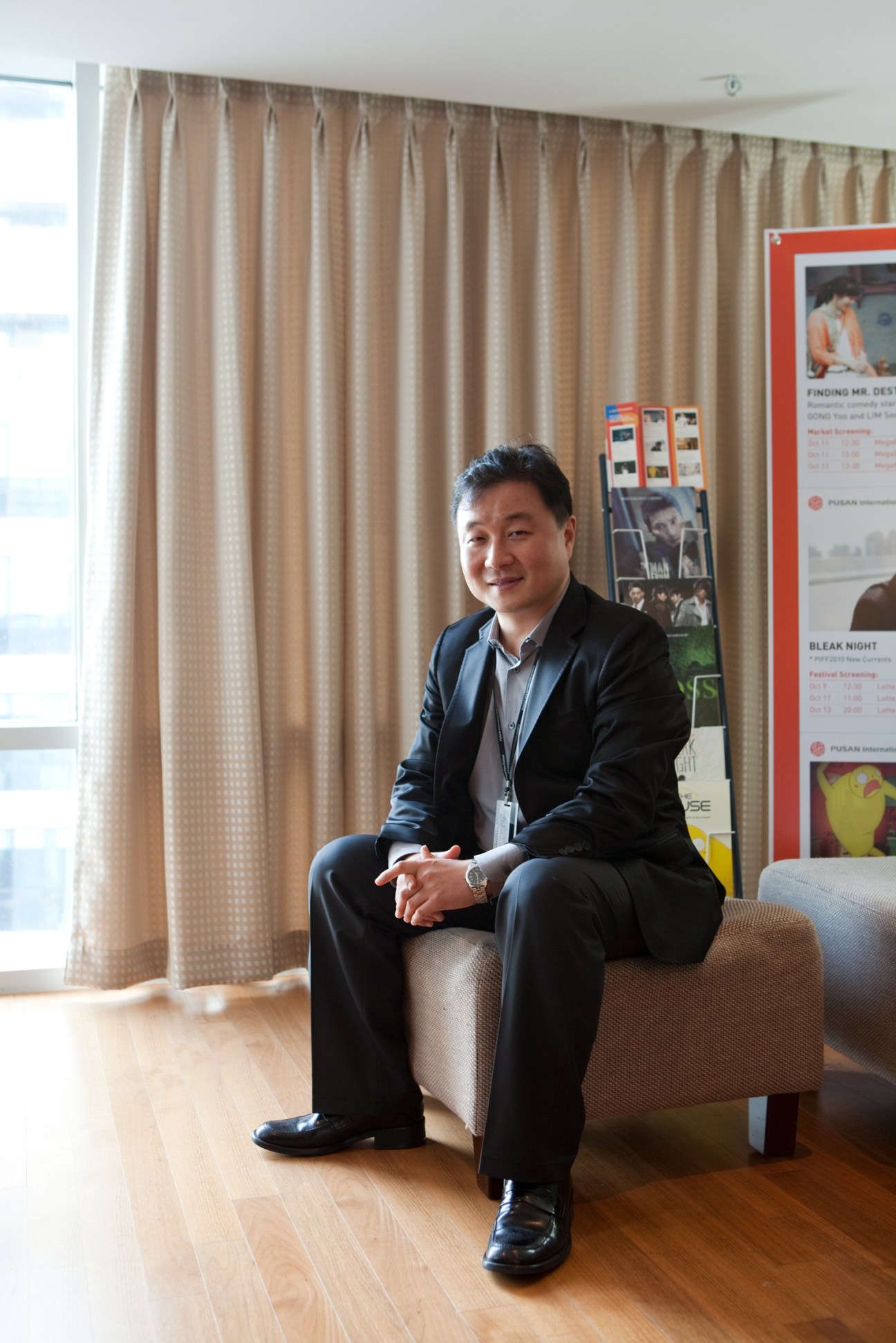 Kini Kim, senior vice president of CJ Entertainment, sits on a beige ottoman in a hotel room with film festival posters on the wall behind him.