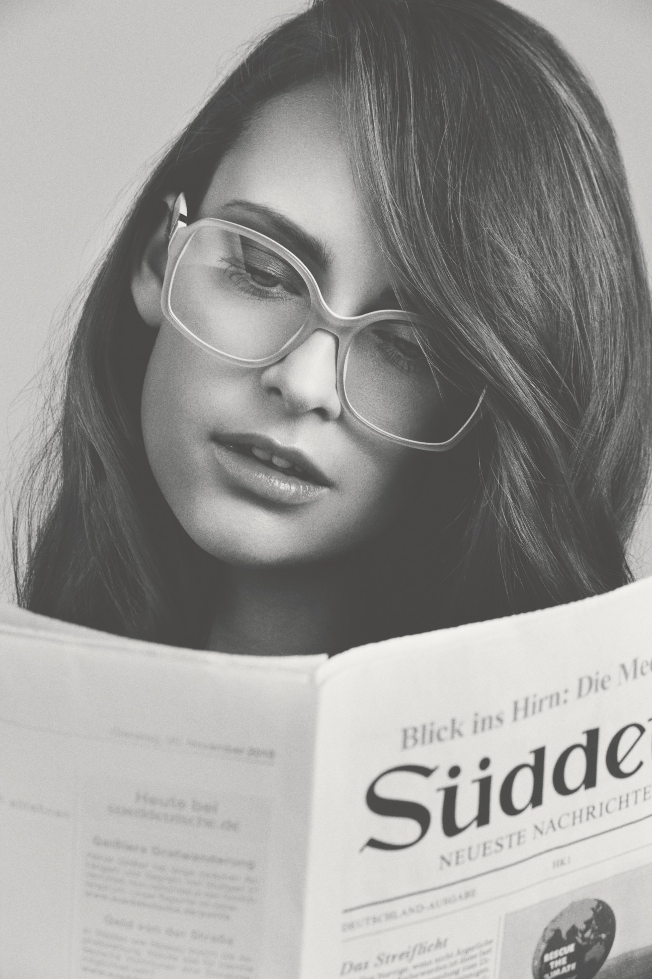 Woman wearing Prada VPR-12N glasses reading a newspaper in black and white.