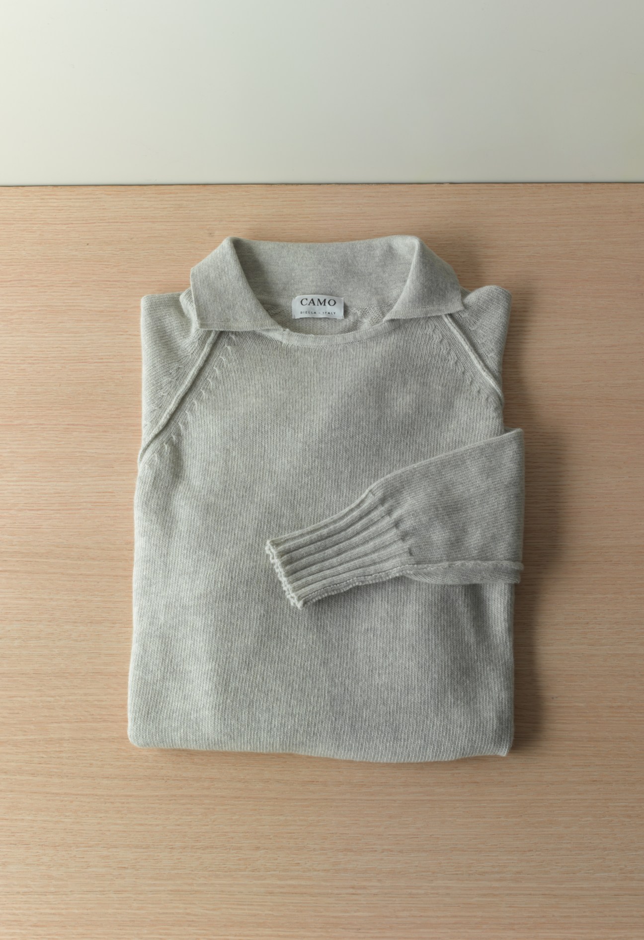 Grey ribbed sweatshirt by Camo with crew neck and striped cuff detail, folded flat on wood surface.